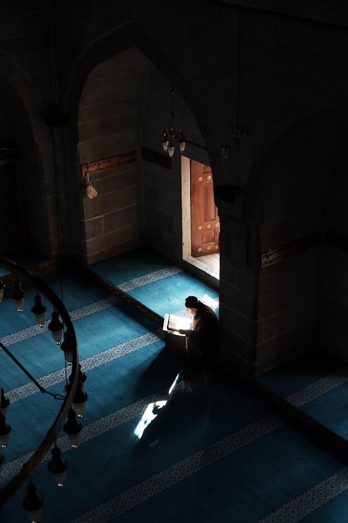 A man reads the Quran in a serene mosque interior with sunlight streaming through the door.